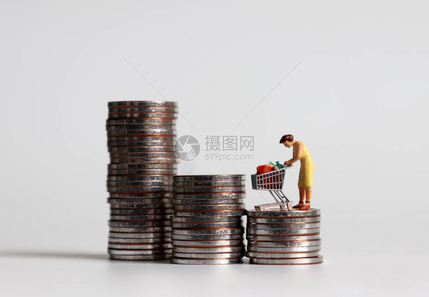 一位迷你女人拿着一辆购物车站在三堆硬币上图片