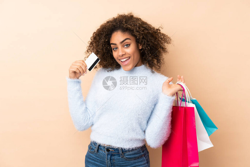以米色为背景持有购物袋和信用卡的非洲裔年轻美裔女子被图片