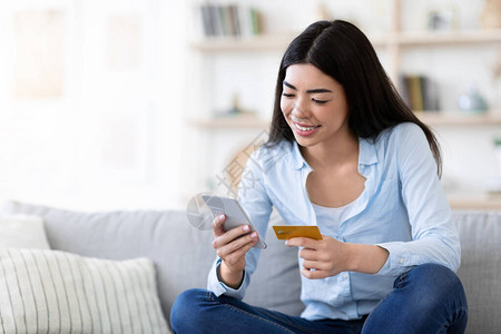 快乐的亚洲女在家使用智能手机和信用卡上的应用程序图片