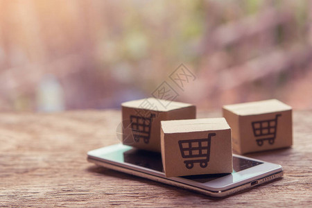网上购物纸盒或木桌上有购物车标志和智能手机的包裹网上购物服务并提供图片