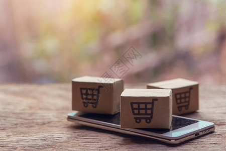 网上购物纸盒或木桌上有购物车标志和智能手机的包裹网上购物服务并提供图片