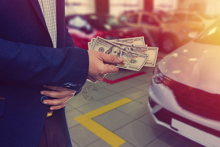 在汽车店卖汽车的推销员或手里拿着美元背景图片