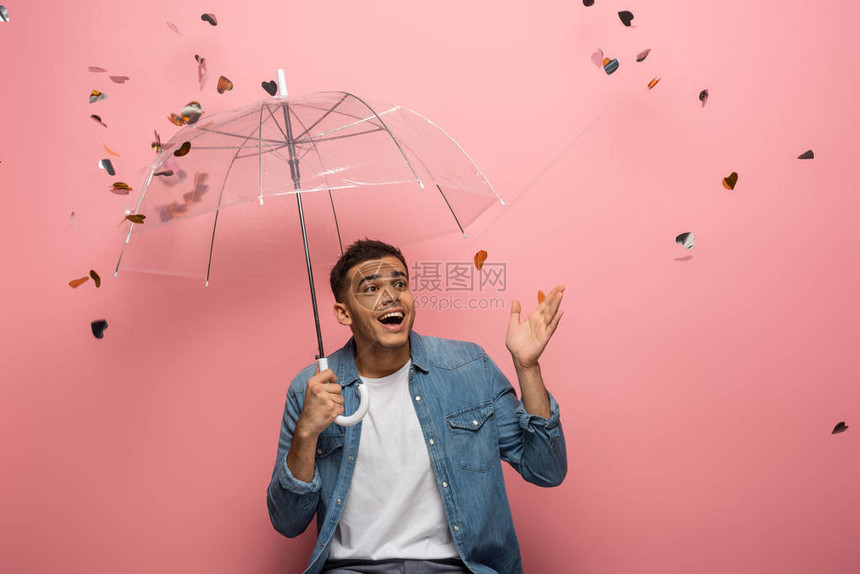 带着雨伞的惊喜男人用手指着在粉红背景上掉下图片