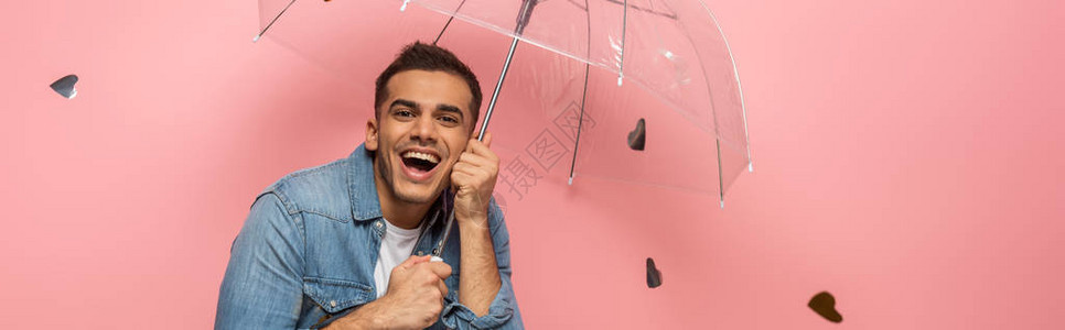 光彩照耀着快乐的男人带着透明的伞在粉红背景的面图片