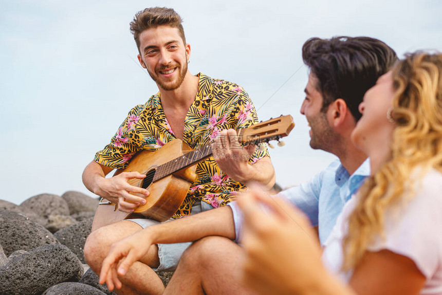 一群快乐的朋友在海边玩吉他和唱歌夏季和假期人们的生活方式概念专图片