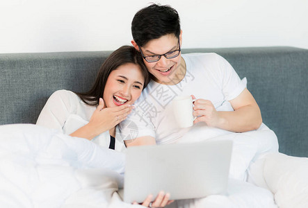 年轻一对情侣的爱男女早上在床上看笔记本电脑影快乐时刻的概图片