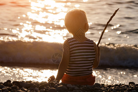小男孩坐在日落的沙滩上拿着一图片