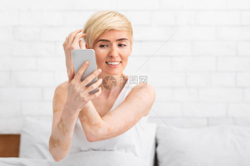 中年妇女摸着头发微笑地着看像照镜子一样的手机图片
