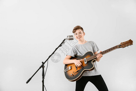 十几岁的男孩弹吉他在浅色背景下唱歌图片