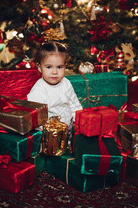 坐在堆红色和绿色圣诞礼物的可爱的白种人小女孩的肖像图片