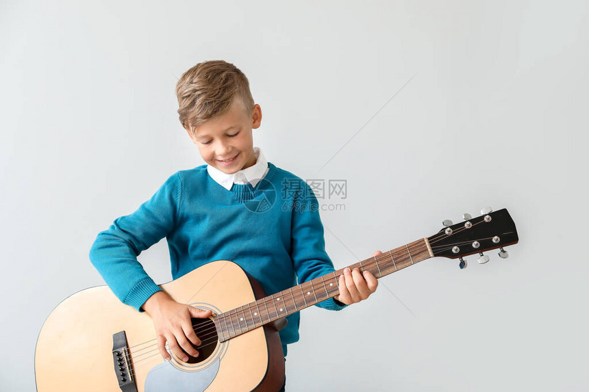 在浅色背景下弹吉他的小男孩图片