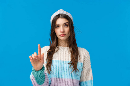 穿着冬季毛衣帽子举起一根手指表示不赞成限制或警告的严肃自信的女人图片