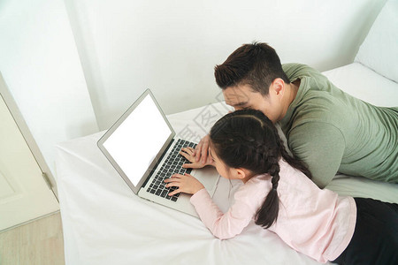 Asian家庭父亲和女儿在家床上使用带白屏幕图片