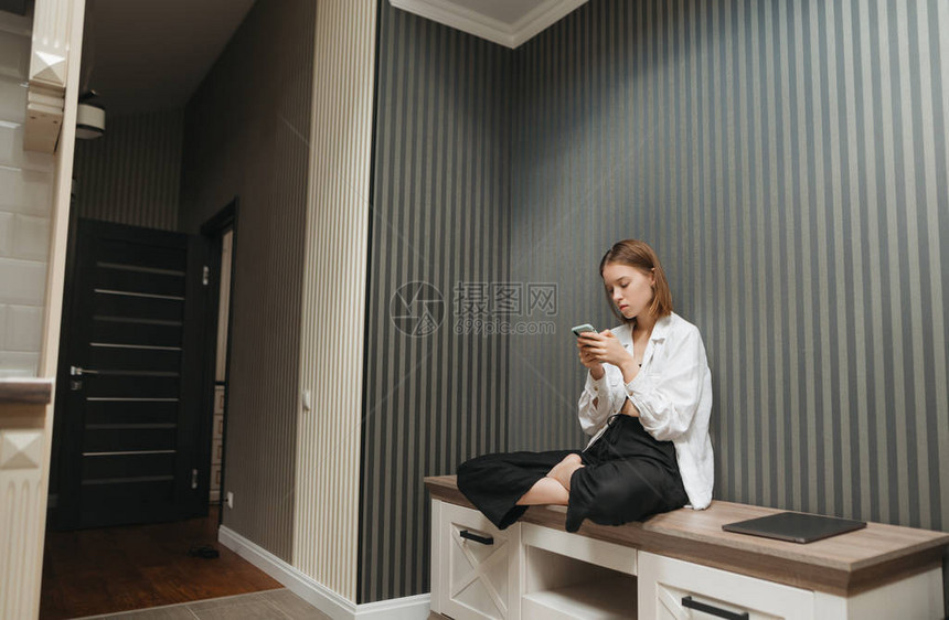 穿着时髦衣服的漂亮女孩在家中坐在公寓的床头柜上图片