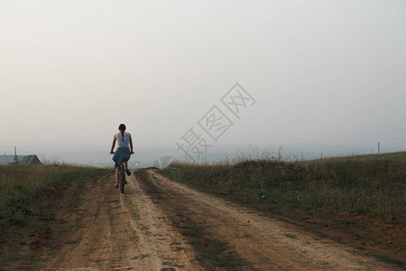 身着休闲服骑自行车在乡村道路上骑自行车的白人年轻女图片