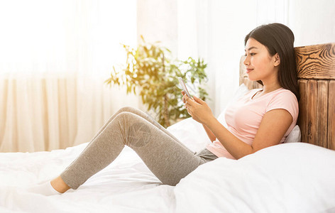 周末在卧室睡觉时使用手机在床上聊天发短信的日本女孩Mobile图片