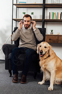 视障男子在家中在金毛猎犬旁边用耳机听音乐图片
