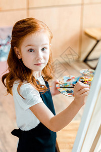 红发儿童持有油漆刷和观看相机的红发儿童图片