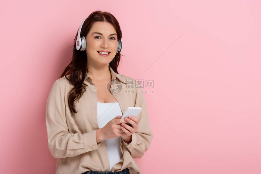 迷人的女子在用耳机和智能手机打粉红背景图片