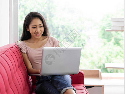 年轻的亚洲青少年在红色沙发上使用笔记本电脑在客厅放松图片