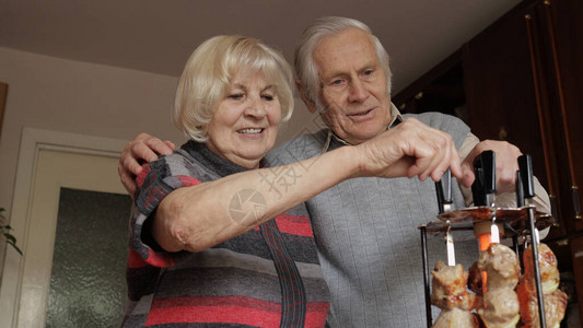 快乐的老成熟退休祖父母夫妇在家里的桌子上享受在电烤架上烹饪烧烤图片
