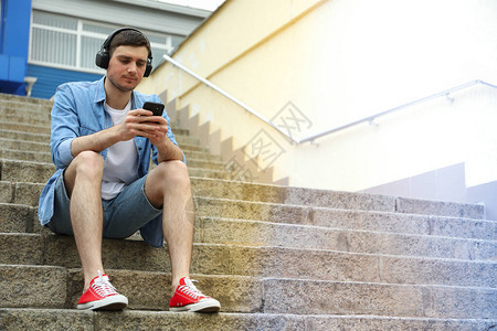 戴耳机的年轻人坐在台阶上看手机图片