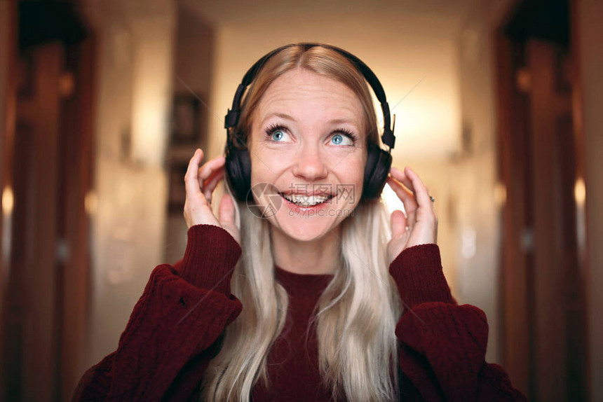 一个年轻快乐的金发女子在家里听无线蓝牙耳机上的图片