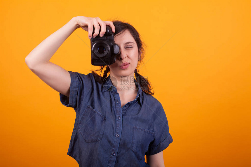 有吸引力的白种女人与照片相机聚焦在黄色背景的工作室摄影师的现代技术摄影工作室女摄影师正在用图片