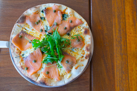 木桌上的木盘上放着美味的烤三文鱼意大利披萨图片