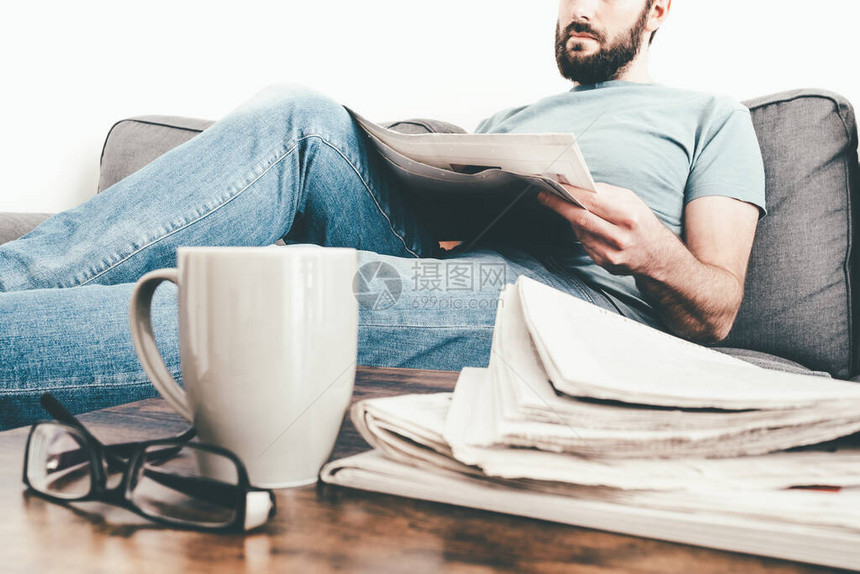 在沙发上放松的男子阅读报纸堆叠着报纸和图片
