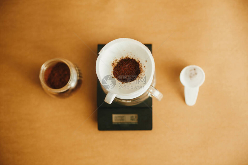 滴咖啡平躺过滤器中的磨碎咖啡倒在棕色背景上的刻度和玻璃杯上酿造芳香新鲜的替代咖啡图片