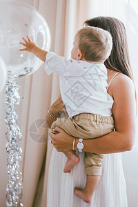 可爱的男婴看着透明的气球在家中与母亲一起在明亮的室内庆祝孩子图片