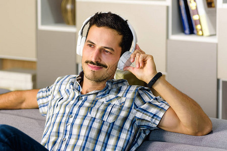 男人在家里舒适的沙发上用立体声耳机放松地听音乐图片