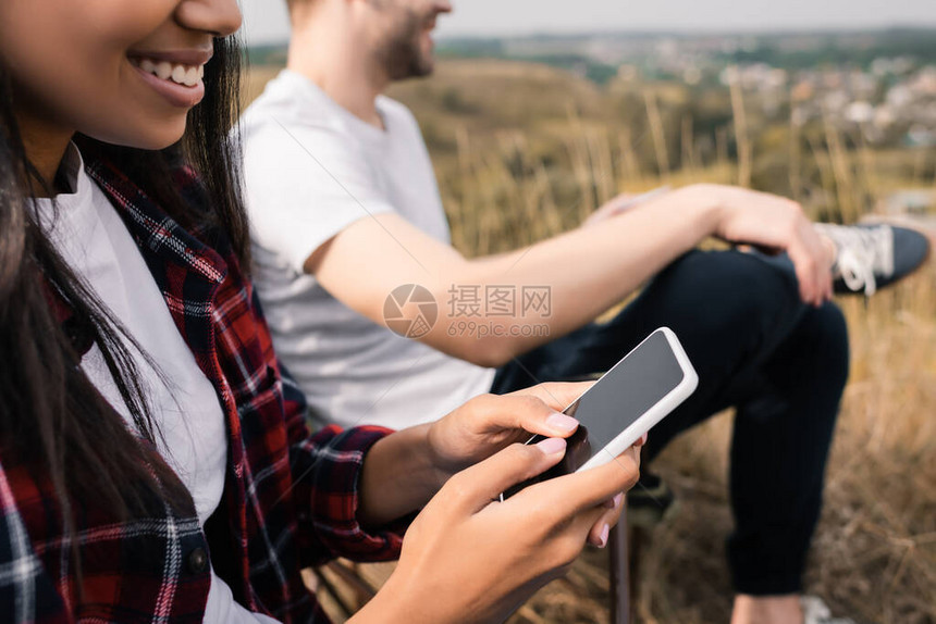 在露营期间使用智能手机与男朋友亲近时背景模糊的非洲女笑着微笑的美裔女图片