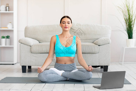 坐在笔记本电脑前和在家放松的在线瑜伽课上冥想的和平女人图片