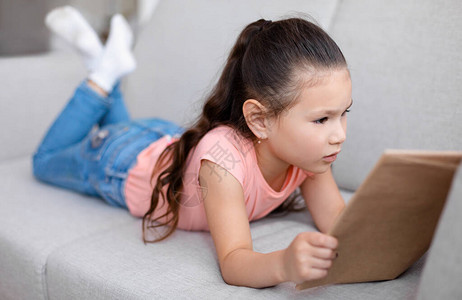 亚洲小女孩在家看书躺在沙发上儿童周末休闲图片