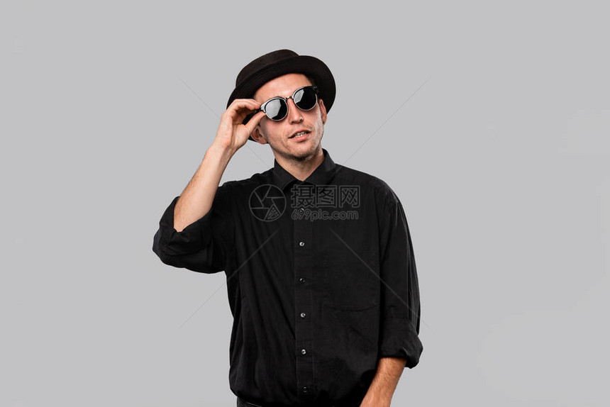 一个穿黑衬衫馅饼和太阳眼镜帽的时髦英俊男子的肖像在灰色图片