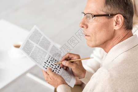 在报纸上拿着铅笔贴近填字游戏的眼镜上高年男子图片