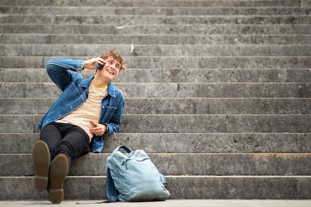 全长的肖像快乐的年轻男子放松在台阶外面与手机图片