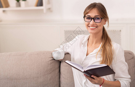 周末快乐的女士阅读书和在家中沙发上放松喝咖啡图片
