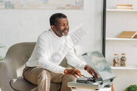 坐在扶手椅上听音乐录音播放机的非洲快乐男人图片
