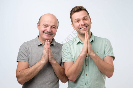 两个英俊的欧洲男人父子手牵在Namaste迎接客人积极的面部人类情感图片