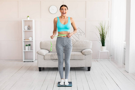 减肥幸福的女人站在家里的体重秤上测量腰围文图片