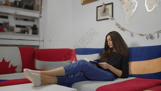 年轻女子在家中的沙发里看纸书坐在图片