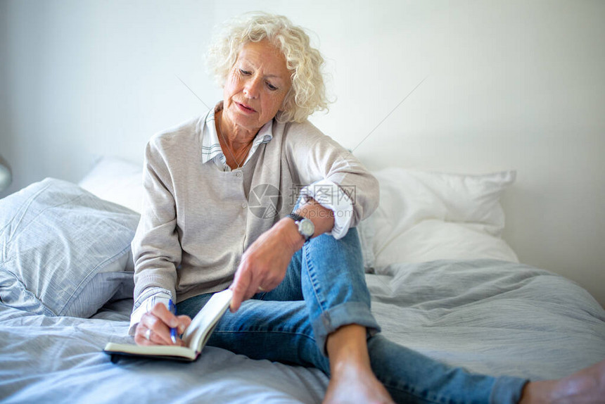 肖像年长的女人坐在床上写日记图片