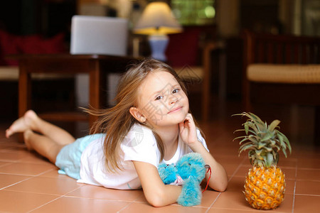 坐在地板上玩菠萝和玩具的小赤脚可爱女孩图片