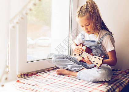 一个小女孩坐在房子的窗边弹吉他选择焦点音乐和艺术的概图片