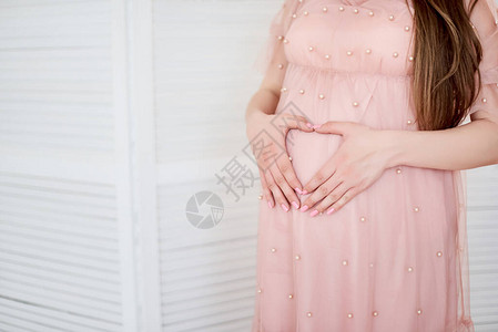 美丽的孕妇以心形拥抱肚子的裁剪图像一名孕妇在前景上抚摸她的腹图片
