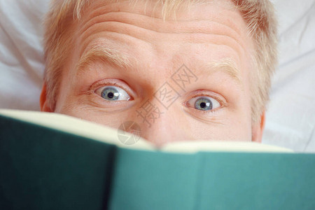 白种人年轻情感开朗的人躺着看书眼睛的特写在家放松阅读有趣的令人兴奋图片