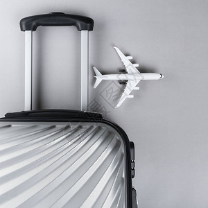 平铺灰色手提箱用灰色背景的小型飞机背景图片